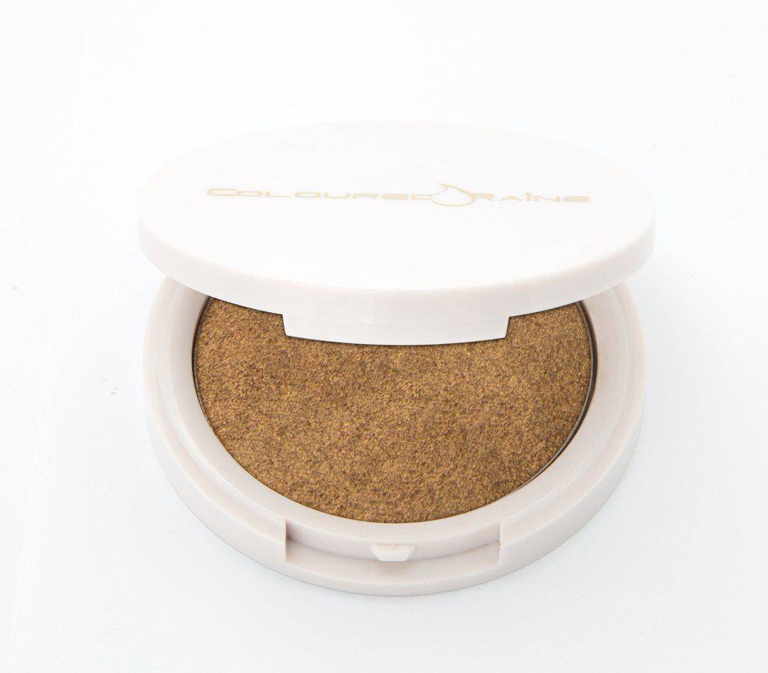 Your Treat - Golden bronze  highlighter by Coloured Raine Cosmetics. Half-open, in a white, circular, mirrored container.